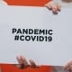Two medical professionals holding up a clipboard that says pandemic #COVID19