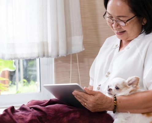 A senior woman snuggling her dog while searching her tablet electronic device for a senior primary care physician