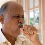 A senior citizen coughing due to his chronic condition, signaling he might qualify for complex care management services